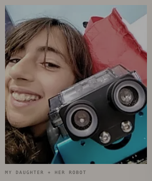 A child holding a small robot up to the camera. Caption on the print: my daughter and her robot.