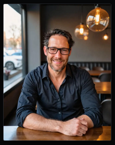 Jesse Kulp seated at a table, smiling, glasses, dark shirt, hands clasped.